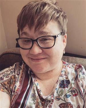 A picture of a white woman with a light brown pixie cut and glasses is smiling at the camera.